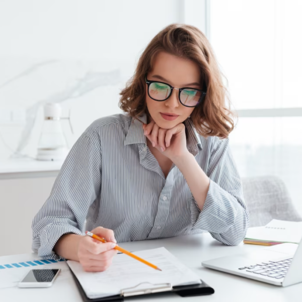 concentrated woman in glasses and striped shirt working with papers and laptop