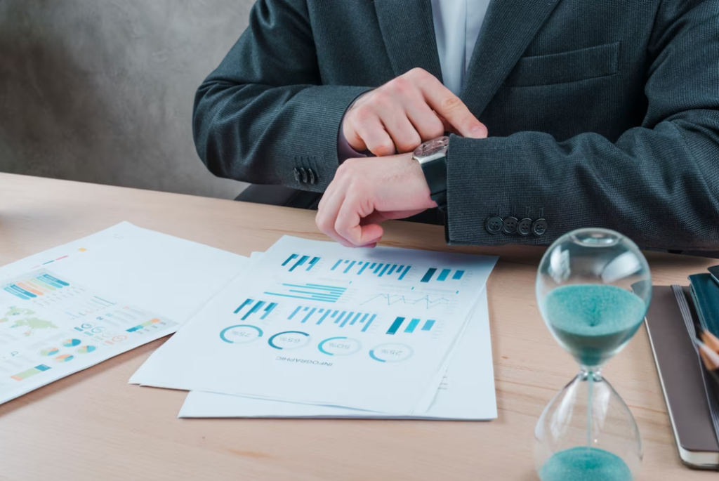 man in the office sitting at the table watching at his watch and papers with diagrams