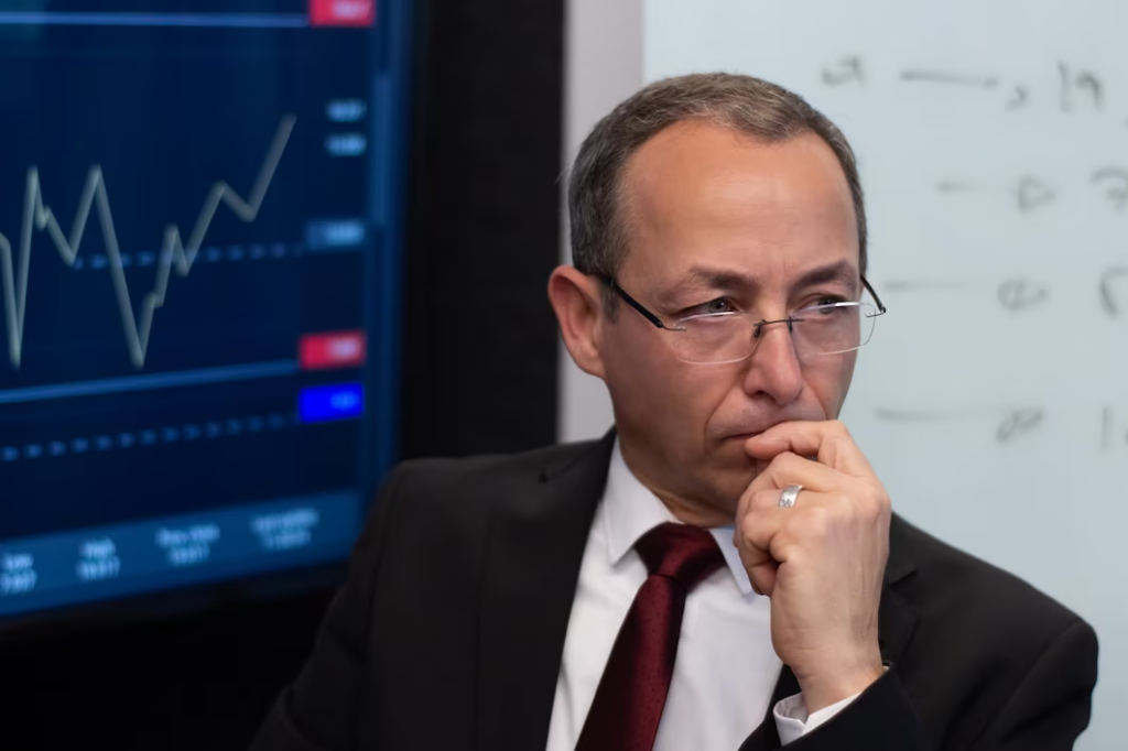 Man wearing a suit, with his hand on his mouth in a thoughtful pose, and wearing eyeglasses